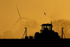 Farmer plants milo in his field as wind turbines rise in the distance